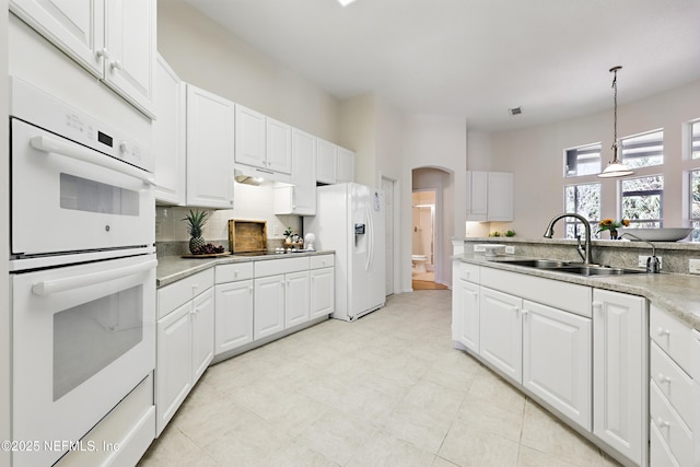 kitchen featuring light countertops, arched walkways, white cabinets, white appliances, and a sink