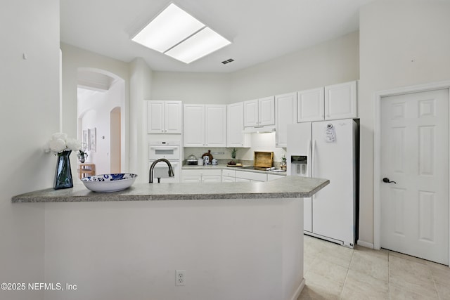 kitchen featuring under cabinet range hood, white cabinetry, white appliances, arched walkways, and a peninsula