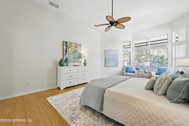 bedroom with visible vents, ceiling fan, baseboards, light wood-style flooring, and a towering ceiling