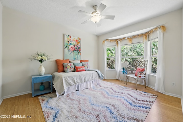 bedroom with ceiling fan, wood finished floors, baseboards, and a textured ceiling