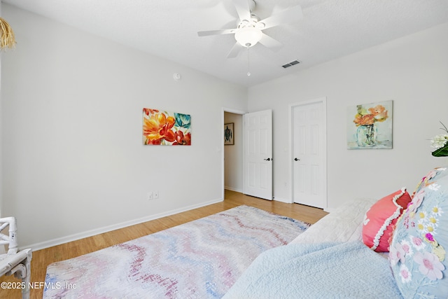 bedroom with ceiling fan, wood finished floors, visible vents, and baseboards