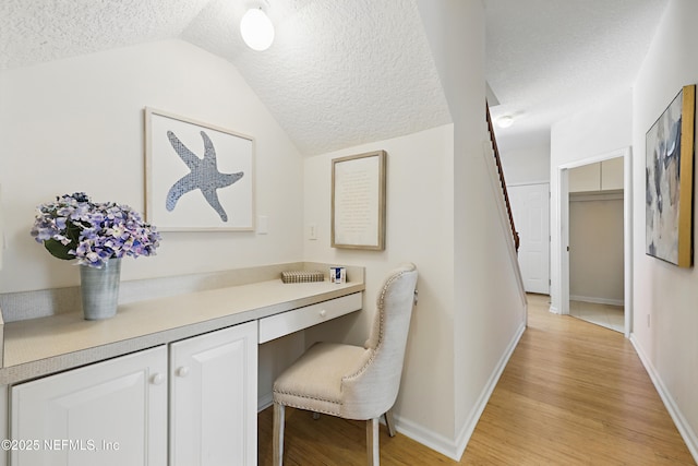 office space with lofted ceiling, light wood-style flooring, a textured ceiling, baseboards, and built in study area