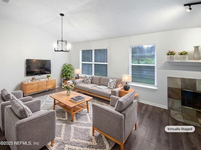 living area with dark wood-type flooring, visible vents, baseboards, a tiled fireplace, and an inviting chandelier