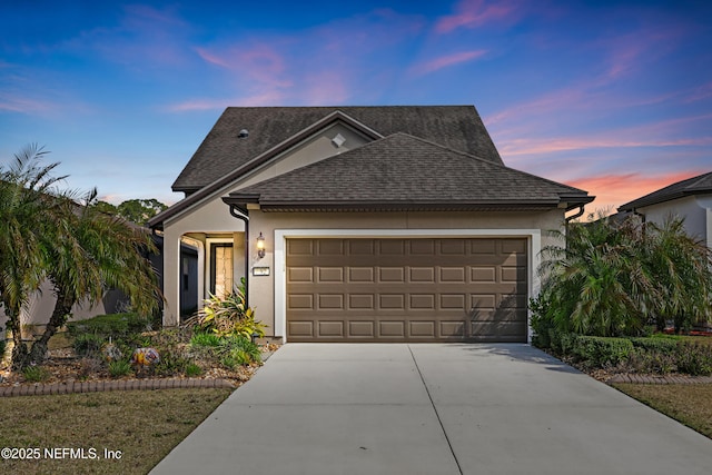 view of front of home with driveway, a shingled roof, a garage, and stucco siding