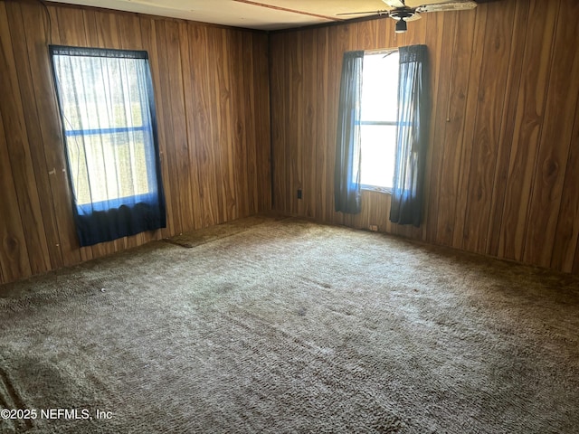 carpeted spare room featuring wood walls and a ceiling fan