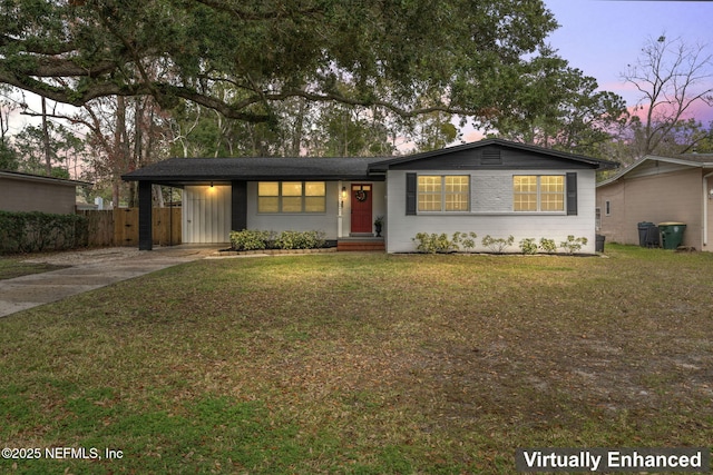 ranch-style house featuring concrete driveway, fence, a carport, and a yard