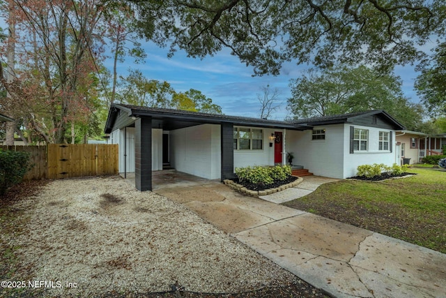 view of front of home with driveway, concrete block siding, an attached carport, a gate, and fence