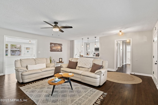 living room featuring dark wood-style floors, ceiling fan, baseboards, and a textured ceiling