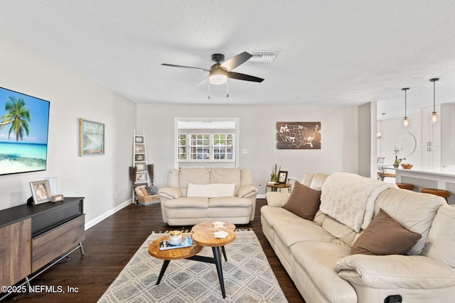 living area featuring dark wood-style floors, ceiling fan, baseboards, and a textured ceiling