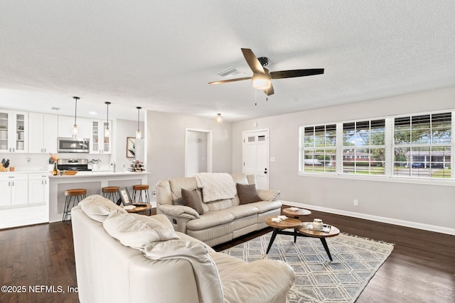 living room featuring ceiling fan, a textured ceiling, baseboards, and dark wood-type flooring