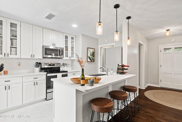 kitchen with visible vents, a kitchen breakfast bar, stainless steel appliances, a textured ceiling, and light countertops