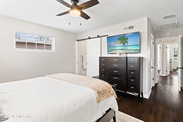 bedroom featuring visible vents, dark wood finished floors, a textured ceiling, and a barn door