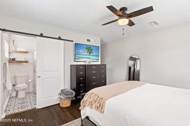 bedroom featuring dark wood-style floors, a barn door, a textured ceiling, and visible vents