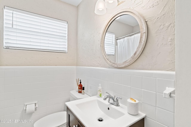 bathroom with toilet, a textured wall, wainscoting, and vanity