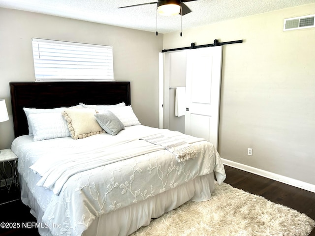 bedroom with a barn door, visible vents, baseboards, a textured ceiling, and wood finished floors