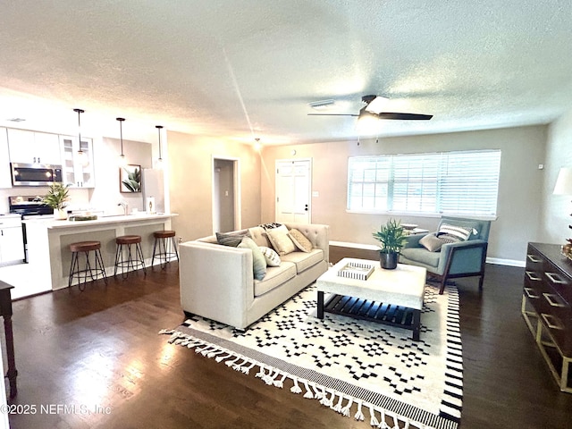 living room with a textured ceiling, ceiling fan, baseboards, and dark wood-type flooring