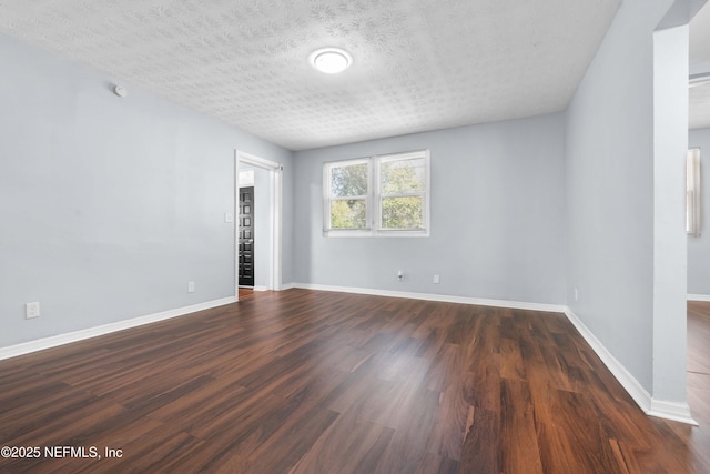 spare room featuring dark wood-type flooring, a textured ceiling, and baseboards