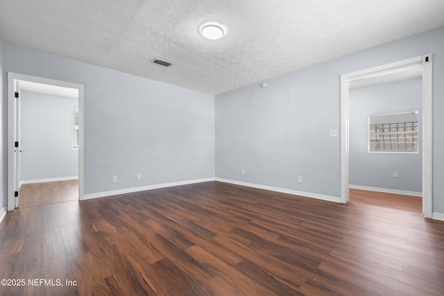 unfurnished room with baseboards, dark wood finished floors, and a textured ceiling