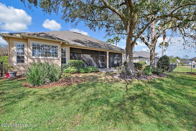 rear view of property with stucco siding, fence, a sunroom, and a yard