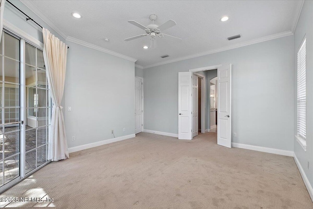 empty room featuring light colored carpet, a ceiling fan, visible vents, baseboards, and ornamental molding