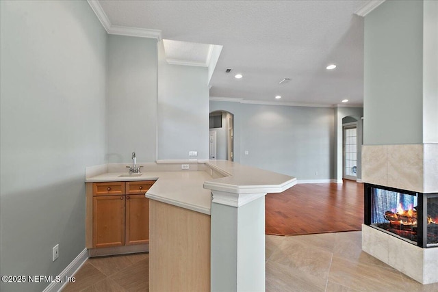 kitchen featuring arched walkways, light countertops, open floor plan, a sink, and a multi sided fireplace