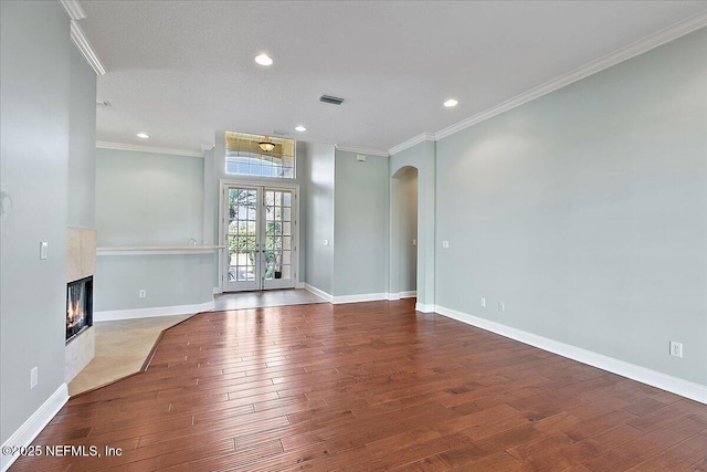 unfurnished living room with baseboards, arched walkways, a glass covered fireplace, wood finished floors, and crown molding