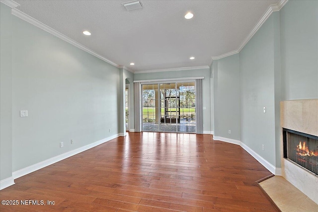 unfurnished living room featuring wood finished floors, visible vents, baseboards, ornamental molding, and a tiled fireplace