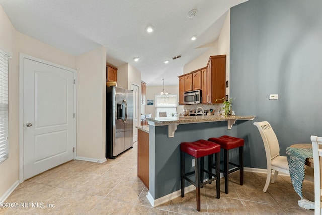 kitchen featuring a breakfast bar area, lofted ceiling, appliances with stainless steel finishes, brown cabinetry, and a peninsula