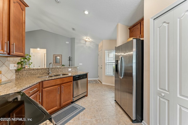 kitchen with lofted ceiling, stainless steel appliances, a peninsula, a sink, and brown cabinets