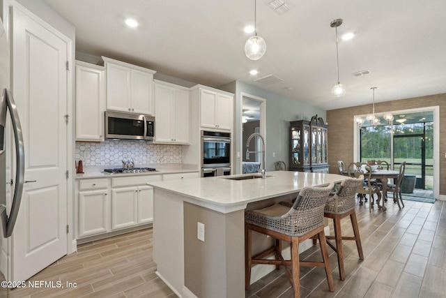 kitchen with a center island with sink, white cabinets, stainless steel appliances, pendant lighting, and a sink