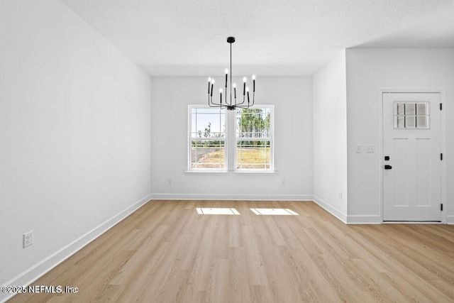 unfurnished dining area with light wood finished floors, an inviting chandelier, and baseboards