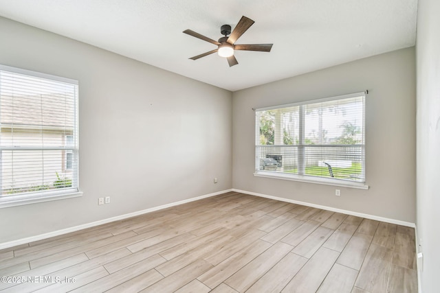 empty room featuring a ceiling fan, a wealth of natural light, light wood-style floors, and baseboards