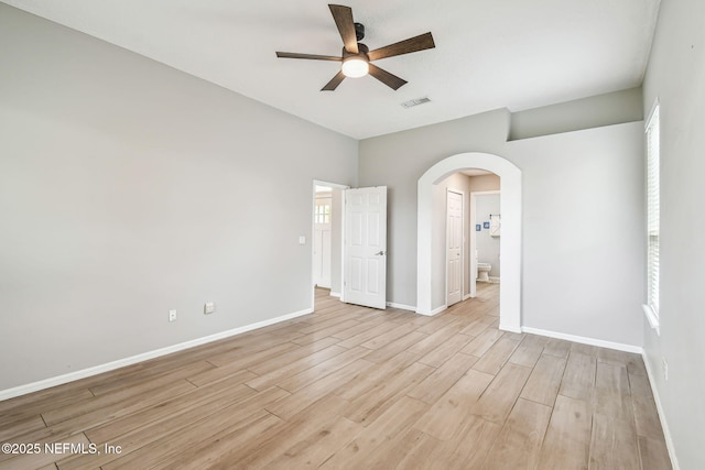 unfurnished room with visible vents, arched walkways, baseboards, ceiling fan, and light wood-style flooring