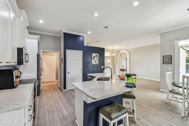 kitchen featuring a breakfast bar, wood finish floors, a sink, white cabinets, and an island with sink