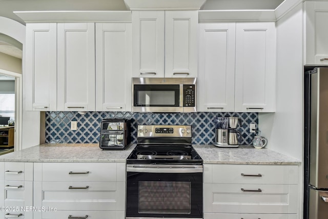 kitchen featuring light stone countertops, white cabinetry, stainless steel appliances, and decorative backsplash