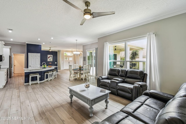 living room featuring a textured ceiling, ornamental molding, light wood-style flooring, and a ceiling fan