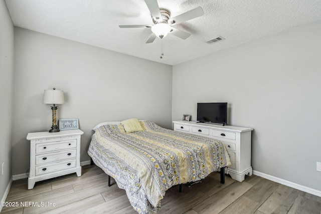 bedroom with light wood-type flooring, visible vents, a textured ceiling, and baseboards