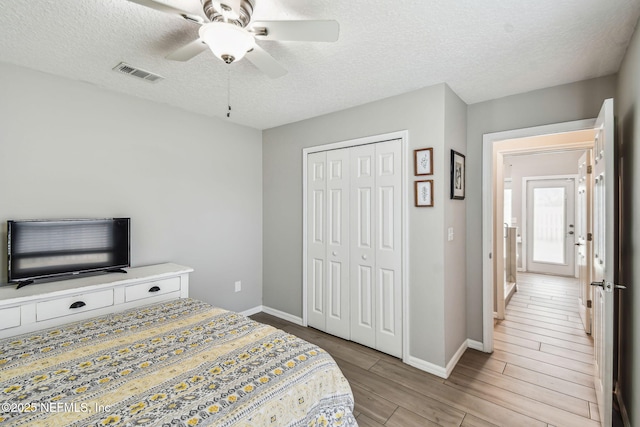 bedroom featuring baseboards, visible vents, a textured ceiling, light wood-style floors, and a closet