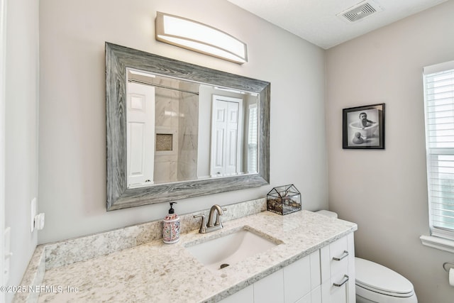 bathroom with toilet, walk in shower, vanity, and visible vents