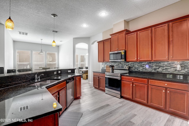 kitchen featuring arched walkways, pendant lighting, stainless steel appliances, backsplash, and a sink