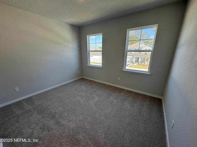 empty room with carpet floors, baseboards, and a textured ceiling