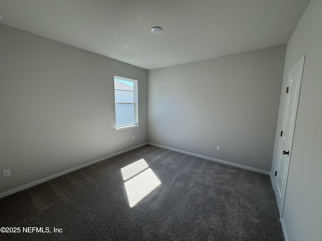 empty room featuring baseboards and dark colored carpet