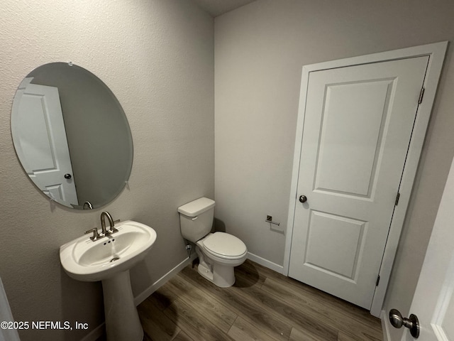 half bathroom featuring baseboards, toilet, and wood finished floors