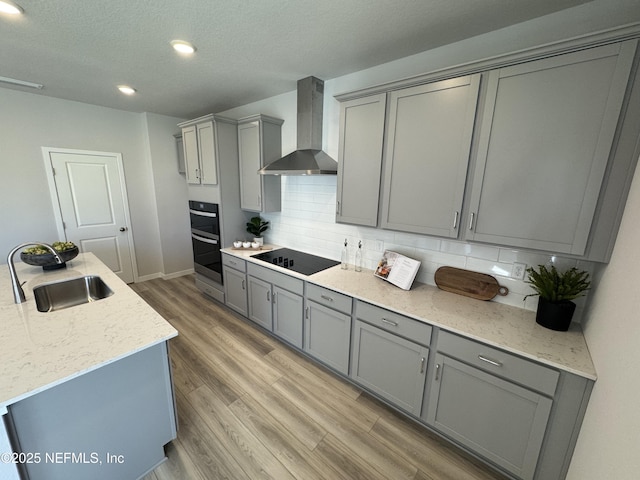 kitchen with decorative backsplash, black electric stovetop, gray cabinets, wall chimney range hood, and a sink