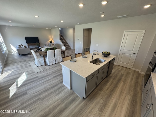 kitchen featuring light stone counters, a center island with sink, stainless steel dishwasher, open floor plan, and a sink