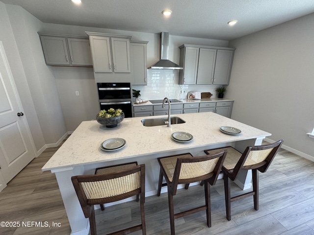 kitchen featuring a sink, wall chimney range hood, gray cabinets, and a kitchen island with sink