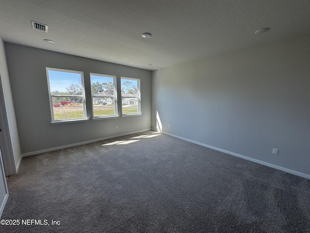 unfurnished room with a textured ceiling, carpet flooring, visible vents, and baseboards