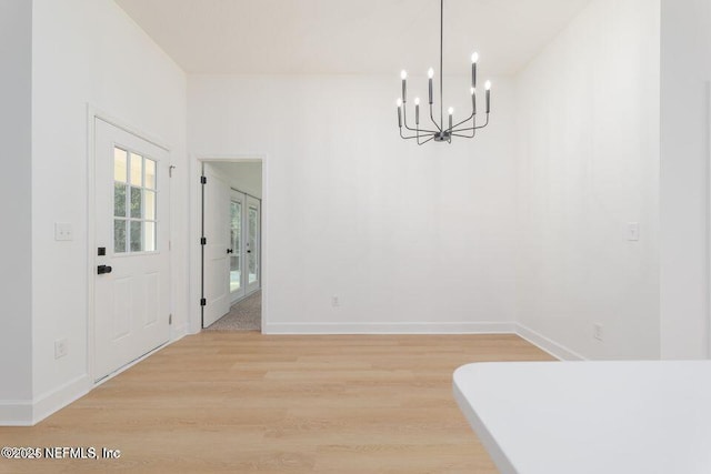 unfurnished dining area featuring an inviting chandelier, light wood-style flooring, and baseboards