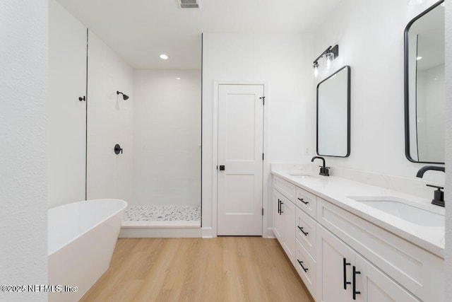 bathroom with a stall shower, a freestanding tub, a sink, and wood finished floors