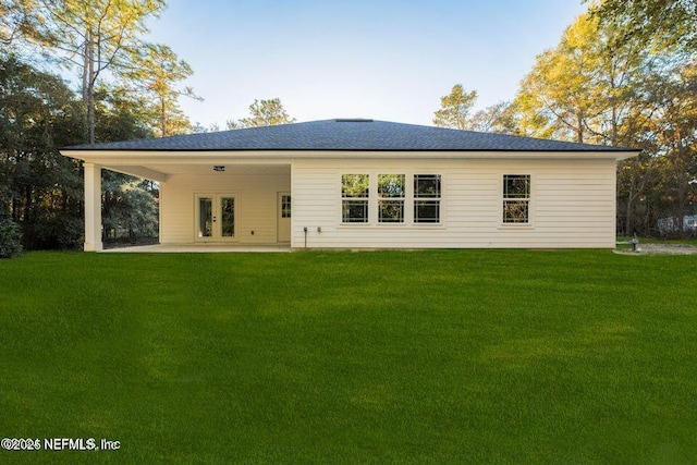 rear view of property with a shingled roof, a lawn, and a patio